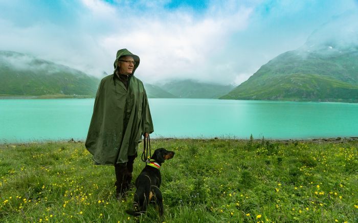 A man next to his dog on the shore of a lake.